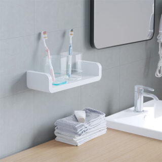 Une petite étagère murale banche en forme de U sur laquelle repose deux verres avec des brosses a dent dedans. En dessous on peut voir une pile de serviettes ainsi qu'un miroir et un lavabo sur la droite