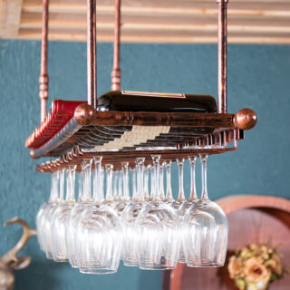 On voit une grande étagère à vin sur laquelle sont posées des bouteilles de rouge et sous laquelle sont suspendus des verres à pied.