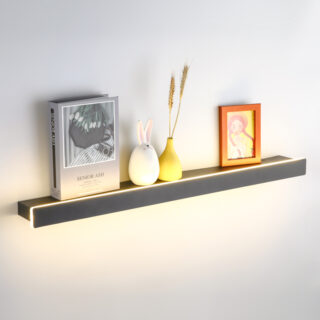 Une étagère murale noire fine éclairée par un bandeau LED sur mur blanc, sur laquelle sont posés un livre, un cadre et deux petits vases colorés.