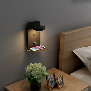 Une petite étagère murale avec support pour téléphone et USB et lampe fixée sur un mur sombre dans une chambre à coucher au-dessus de la table de chevet.