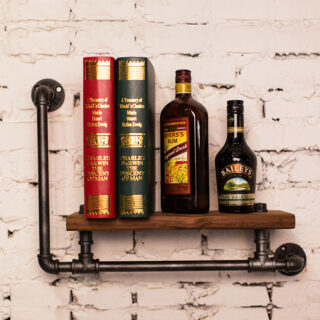 Livres et bouteilles d'alcool posés sur une étagère en bois avec des tuyaux, fixée au mur.