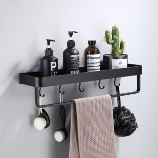 Etagère murale noire en aluminium pour salle de bain avec une barre pour suspendre une serviette et des crochets en dessous pour des gants. Des flacons sont posés sur l'étagère avec un cactus en pot tout à droite. Une serviette beige est suspendue sur la barre et une fleur de douche noire et des brosses sont suspendues sur les crochets.
