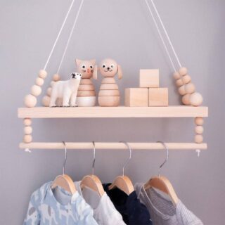 Une étagère suspendue en bois avec des perles en bois et une barre de penderie, avec des jouets en bois posés sur la tablette et quatre habits d'enfants accrochés à des cintres.