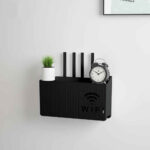 Sur un mur blanc, on voit une étagère noire qui permet de dissimuler votre boxe wifi et de poser des accessoires de décoration dessus.