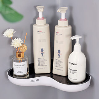 petite étagère d'angle de douche en plastique blanc avec intérieur noir en suspension dans un coin gris avec 3 flacons à poussoirs avec un petit vase à parfum dessus.