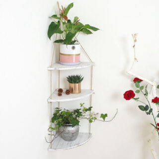 étagère murale d'angle suspendue en bois et corde sur trois étages avec des pots de fleurs dessus.