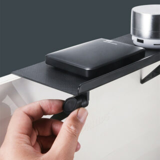 Étagère de rangement moniteur télé posée sur un écran de télévision et tenue par une main à gauche de la photo. Deux accessoires électroniques sont posés sur l'Étagère de rangement moniteur télé