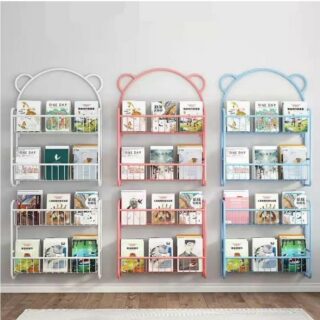 Trois étagères murales en métal avec des livres rangés. De gauche à droite, blanche, rose et bleue. Le haut de l'étagère est arrondie avec des petites oreilles. Les étagères sont deux parties. Sur mur blanc.