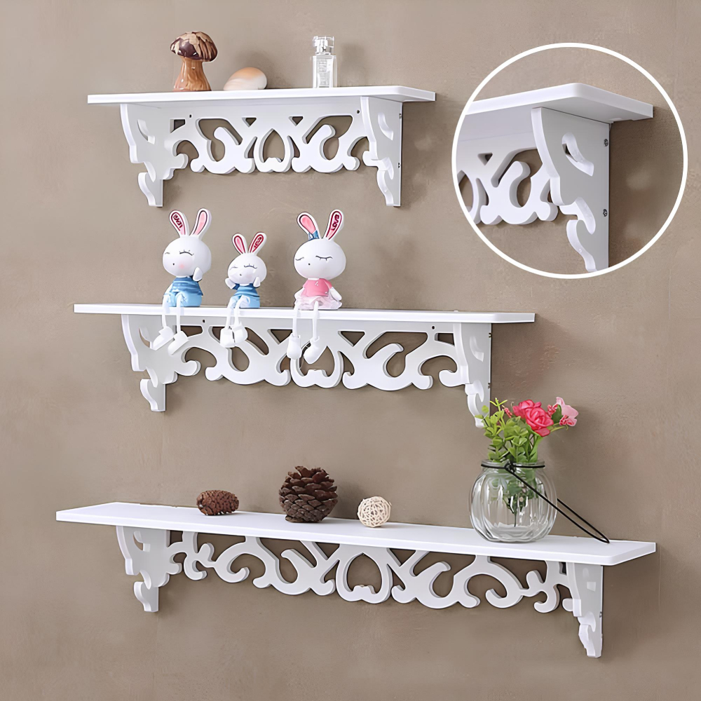 Trois étagères murales rectangulaires avec un design d'arabesques en bois sculpté sous l'étagère. Les trois étagères sont de tailles différentes, de la plus petite en haut à la plus longue en bas. Elles sont chacune des objets de décoration dessus.Fixées sur un mur marron clair. En haut à droite, une bulle montrant en gros plan, le design d'un angle de l'étagère.