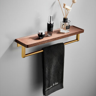 Étagère murale de salle de bain avec une tablette en bois foncé rectangulaire et une barre en dessous en métal dorée où une serviette noire est suspendue. Sur la tablette, un pot de parfum d'ambiance, un flacon et un pot de crème. Sur un mur gris.