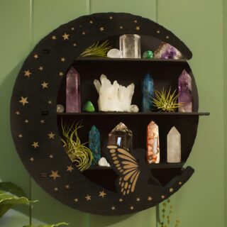 Étagère murale en forme de demi-lune en bois noir avec une fée sur le bas de la lune et des étoiles dorées sur l'ensemble. Au centre, trois niveaux sur lesquels sont exposés des pierres brutes naturelles. Fixée sur un mur vert.