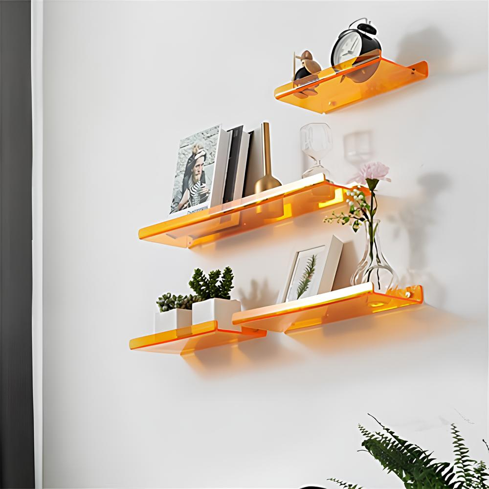Trois étagères murales en acrylique orange avec trois longueurs différentes.Elles se trouvent les unes sous les autres de la plus petite à la plus longue. Elles ont chacune des objets de décoration.