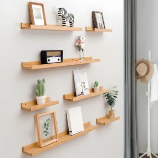 Sept étagères en bois clair avec rebord fixées sur un mur blanc. Différentes longueurs avec des objets de décoration, cadre, photos, plantes artificielles, sur chacune d'entre elles.