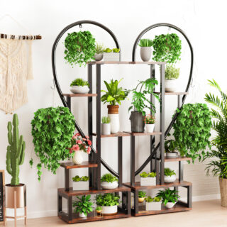Étagère murale posée au sol en forme de cœur en métal noir. Diverses tablettes en bois avec plantes en pot posées dessus. Le mur derrière est blanc et le sol est beige. A gauche, au mur, une décoration en macramé et en dessous un cactus.