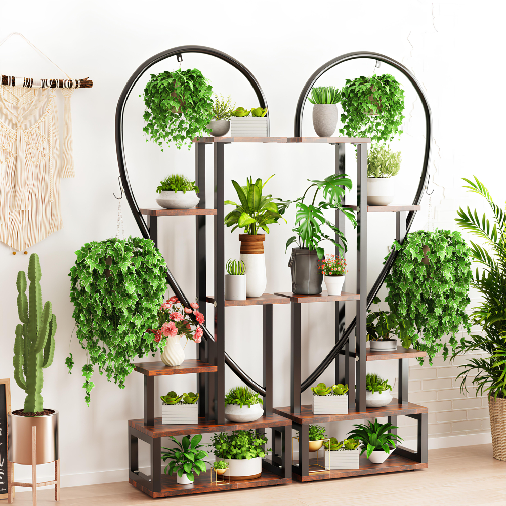 Étagère murale posée au sol en forme de cœur en métal noir. Diverses tablettes en bois avec plantes en pot posées dessus. Le mur derrière est blanc et le sol est beige. A gauche, au mur, une décoration en macramé et en dessous un cactus.