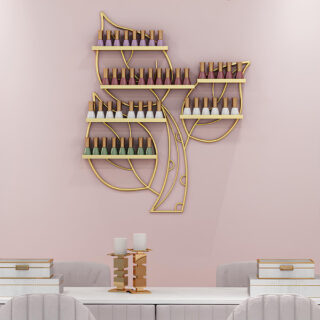 Étagère murale en forme de 3 feuilles dorées sur lesquelles se trouvent des supports avec des vernis de couleur. Fixée sur un mur rose, au-dessus d'une longue table blanche avec des sièges gris.