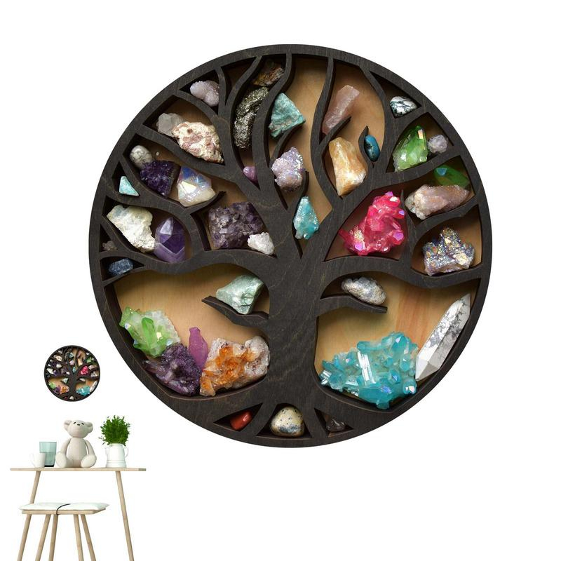 Étagère murale ronde en bois foncé avec un arbre sculpté au centre. De multiples pierres naturelles de couleurs sont placées dans les espaces vides de l'arbre. En bas à gauche, on y voit une table en bois clair avec un tabouret assorti. Sur la table , un pot blanc avec une plante verte, un nounours, un verre vert et une tasse blanche. Au-dessus de la table, la même étagère. Le tout sur fond blanc.