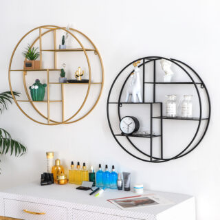 2 étagères murales rondes en métal avec 4 niveaux pour poser des objets de décoration. L'étagère de gauche et dorée, celle de droite est noire. Chacune a des objets dessus. Elles sont fixées sur un mur blanc, au-dessus d'un meuble blanc sur lequel sont posés des flacons au liquide orange et bleu.