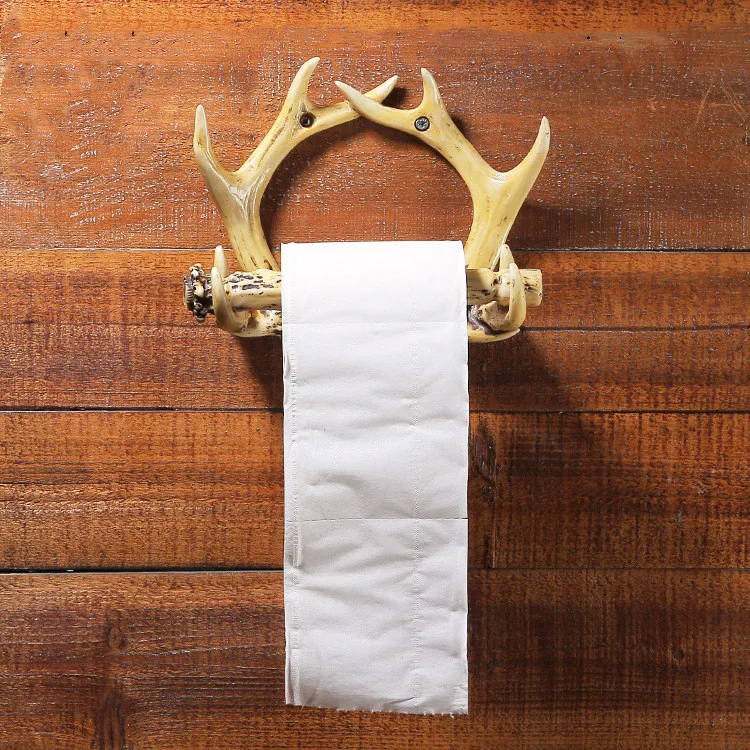 Support mural porte-papier hygiénique en forme de bois de cerf en résine. Un rouleau de papier blanc y est installé. Le support est fixé sur un mur en lattes de bois horizontales marron clair.