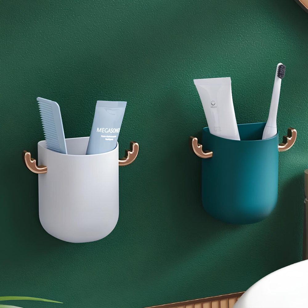 Deux supports en plastique, un blanc à gauche et un vert à droite, fixés sur un mur vert foncé. Chaque support dispose sur les côtés de bois de cerf dorés. Le support blanc a deux tubes de dentifrices et le support vert un tube et une brosse à dent.